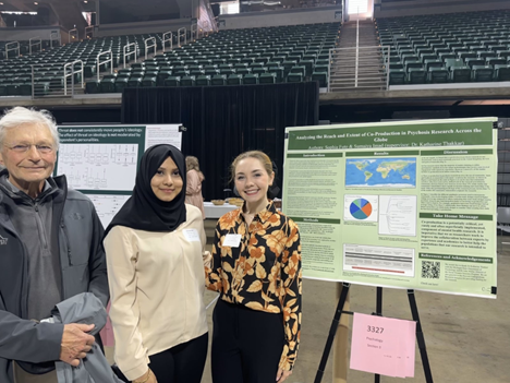 Two women students and one male event participant smile in front of the research poster.