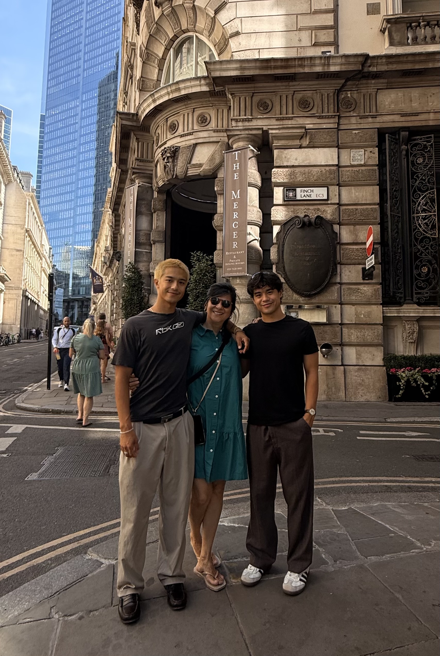 Three people stand with their arms around each other in front of a European building.