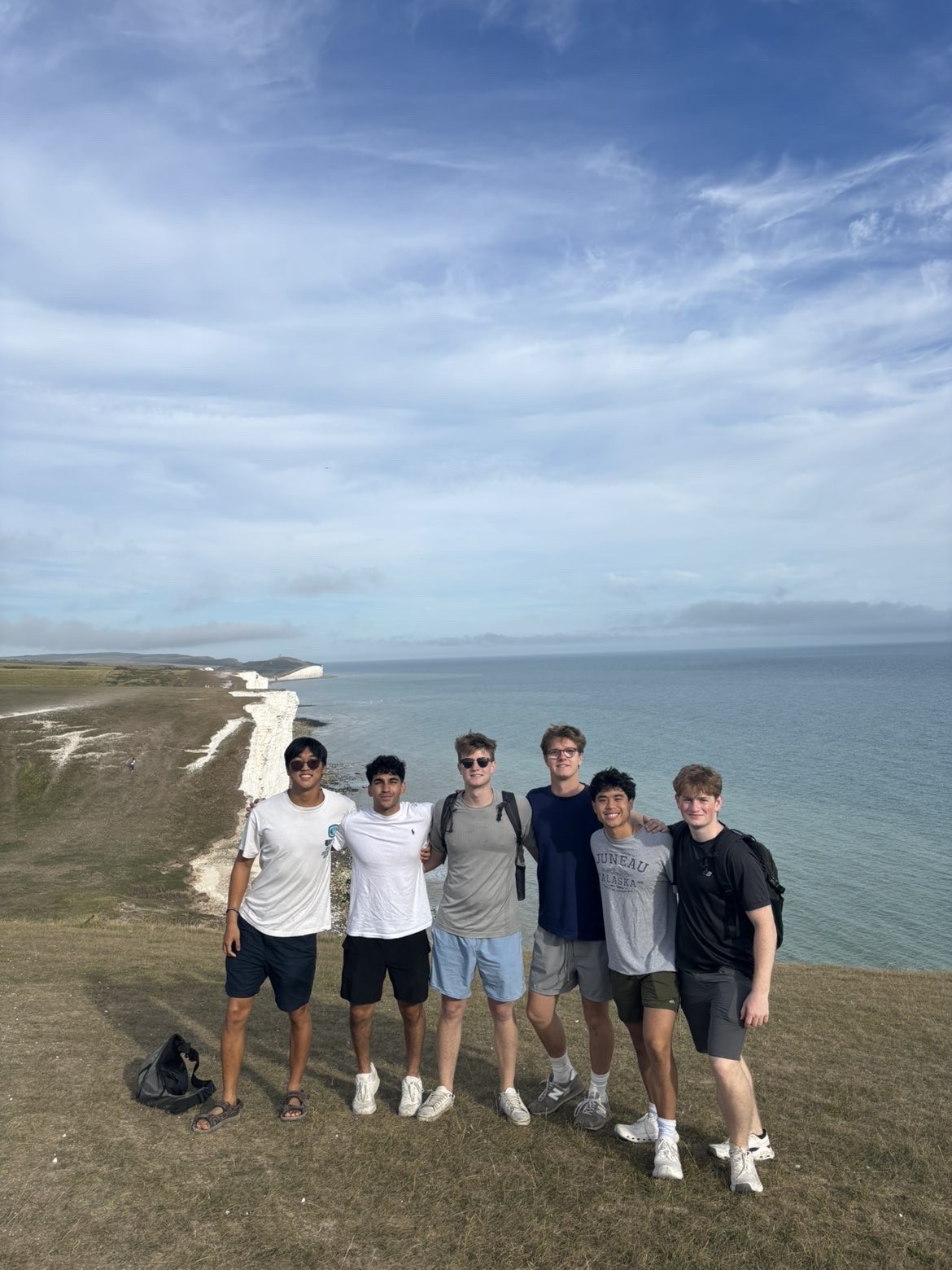Six male students with their arms around each other stand on cliffs with water in the background.