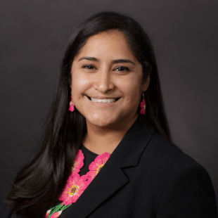Amanda Flores wearing a dark jacket, dark shirt and a bright pink floral beaded necklace. 