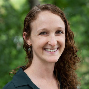 Alexandra Allweiss headshot. Allweiss stands in front of green foliage and smiles for the camera.