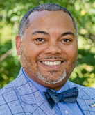 Bryan Beverly headshot. Beverly wears a blue button-down shirt under a blue, plaid blazer and a dark blue bow tie. Beverly's hair is short, black and gray.