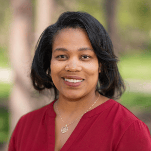 Dorinda Carter Andrews wearing a red shirt with trees and greenery in the background. 