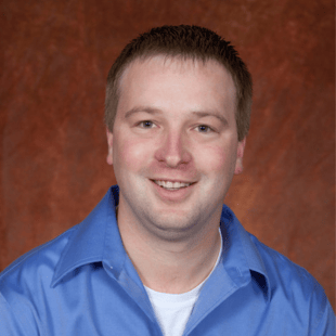 Brad Cox wearing a blue shirt with a warm brown background. 