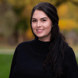 Alexandra Debois wearing a dark sweater. There is fall foliage in the background. 