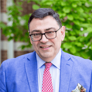Panteleimon Ekkekakis wearing a light blue jacket, red & white pattern tie, and glasses. 