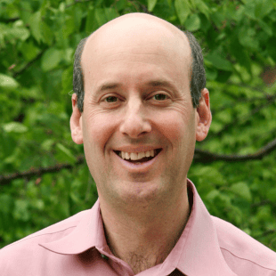 Ken Frank wearing a light red polo with greenery in the background. 