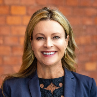 Headshot of Tonya Frisbey wearing a dark jacket and dark shirt with a brick wall backdrop