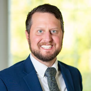 Headshot of Matt Harkey wearing a navy suit jacket, dark tie and white shirt. 