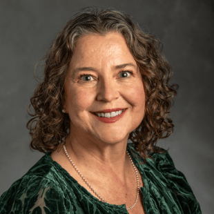 Mary Juzwik wearing a green shirt in front of a gray background. 