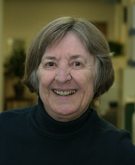 Mary M. Kennedy smiles for the camera in a classroom setting. Kennedy wears a black turtleneck. Kennedy has short gray hair.