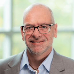 Matthew Koehler wearing a tan jacket, light blue shirt and glasses.