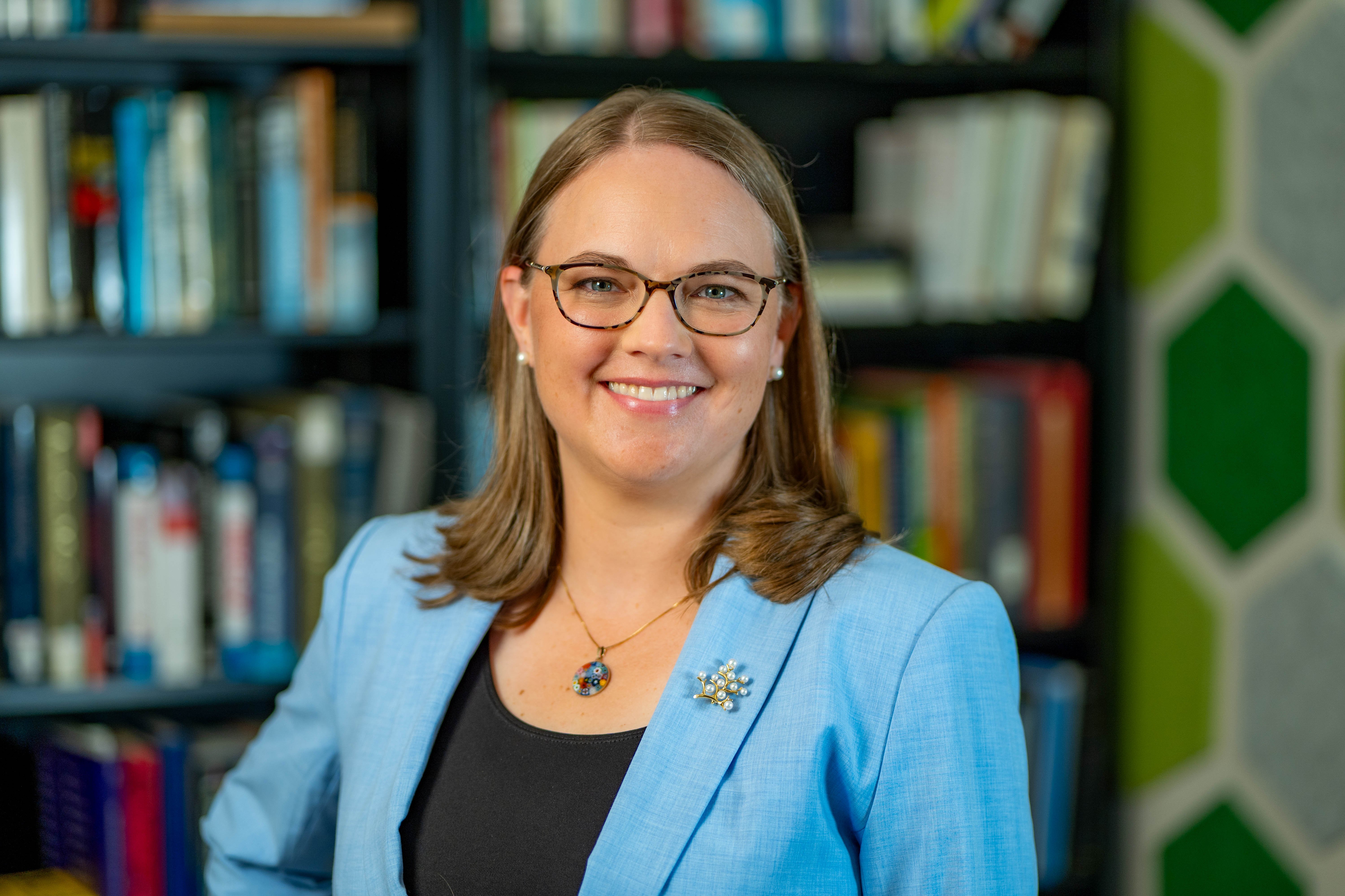 Maddy Mavrogordato wearing a light blue jacket, black shirt and glasses. 