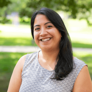 Noreen Naseem Rodriguez wearing a black and white blouse. There is greenery in the background.