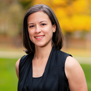 Adrea Truckenmiller wearing a dark blouse. There is fall leaves and greenery out of focus behind her.