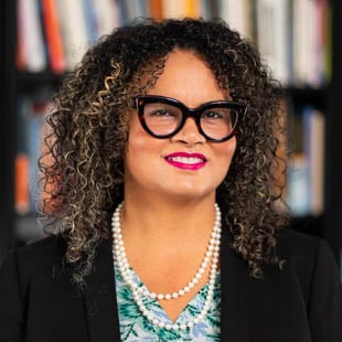 Terah Venzant Chambers wearing a blue top, black jacket and glasses in front of a bookshelf