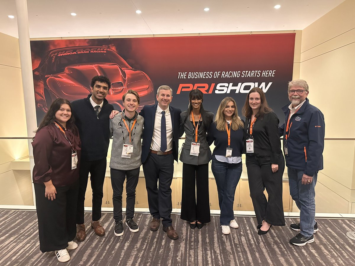 Motorsport researchers gather for a photo at a conference; they stand in front of conference signage.