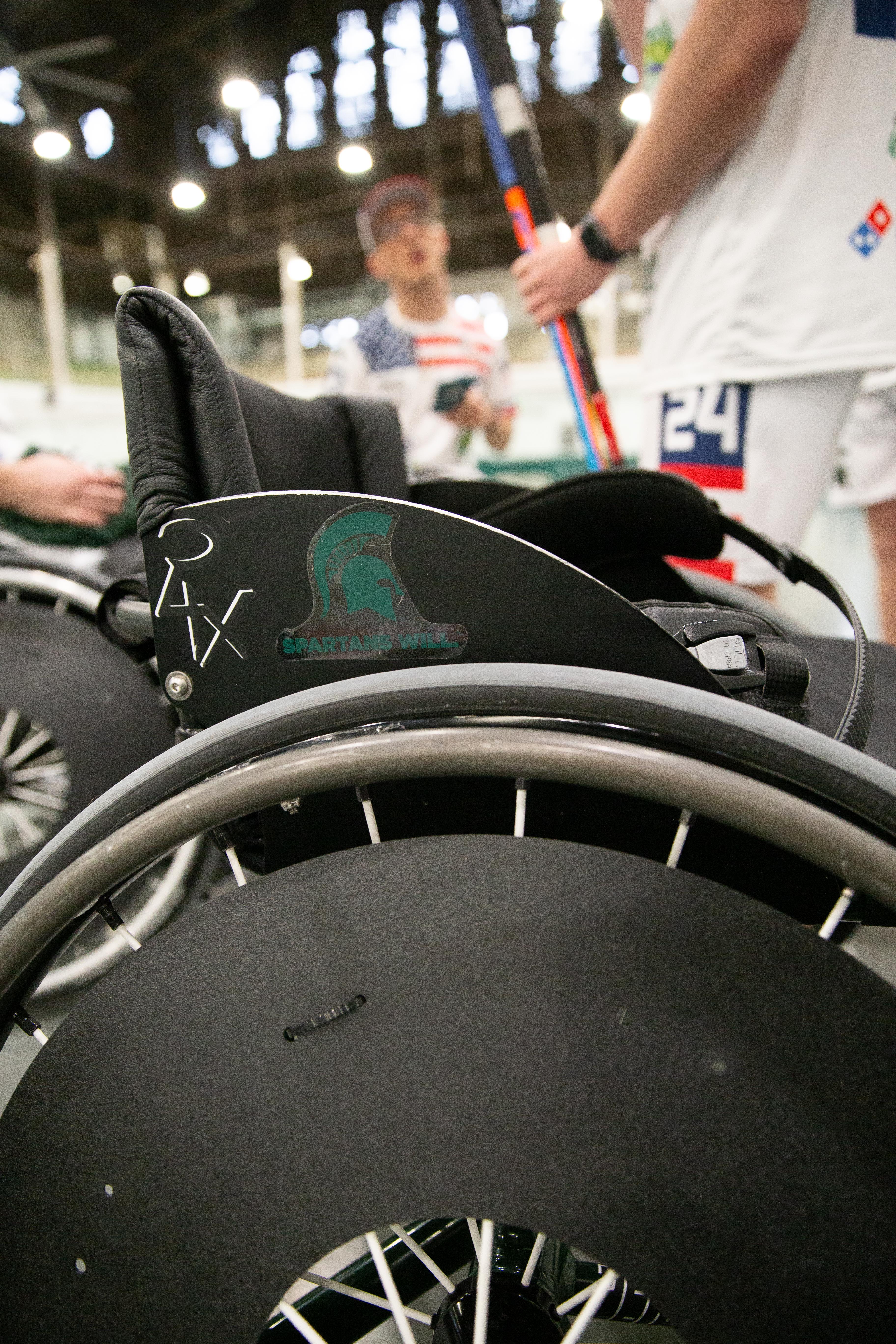 Close-up of adaptive wheelchairs used in various sports contexts. The wheels are dark with a metal exterior frame. An MSU sticker is in the center of the image.