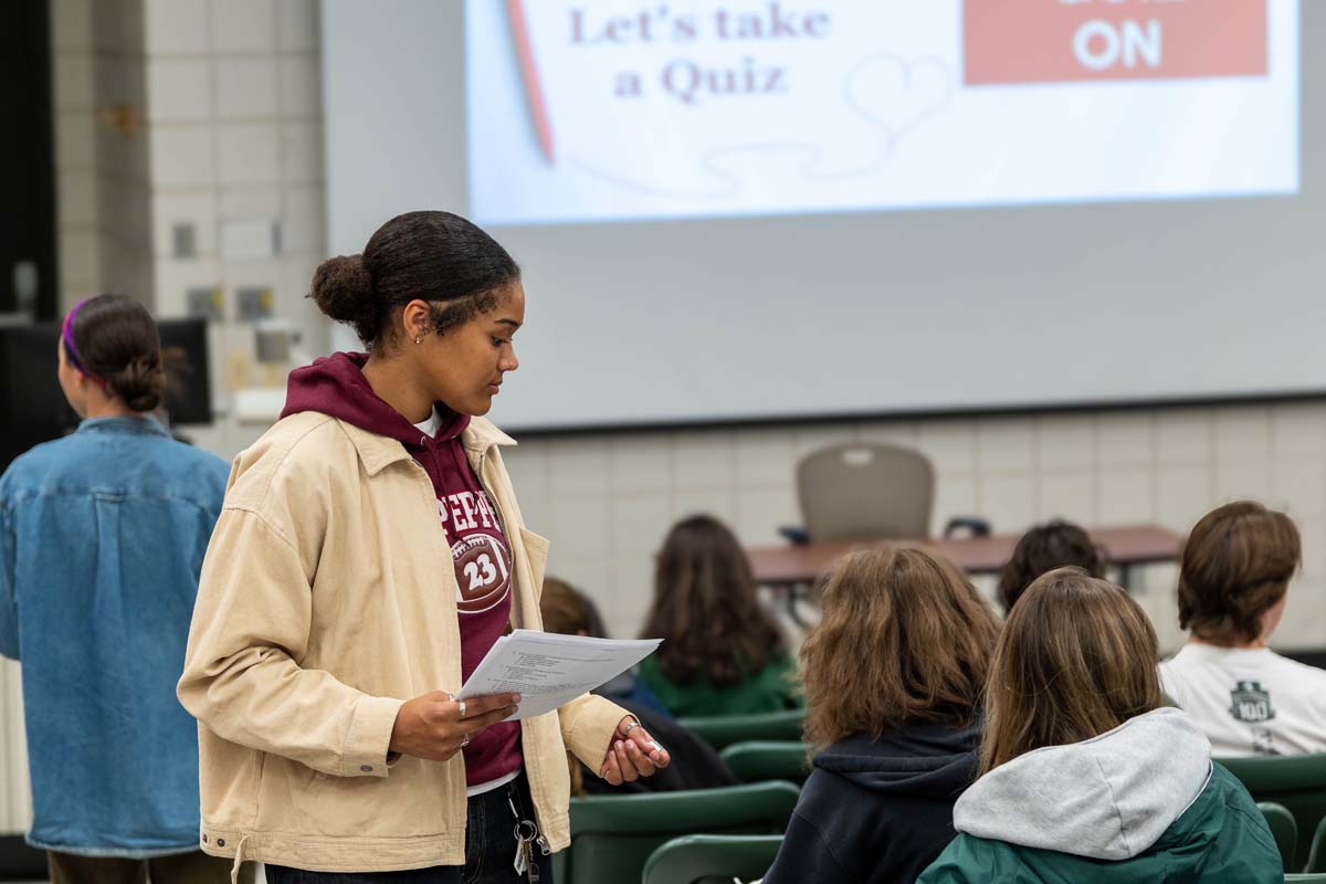 Adriana Canter stands during a class session and collects papers from fellow students.