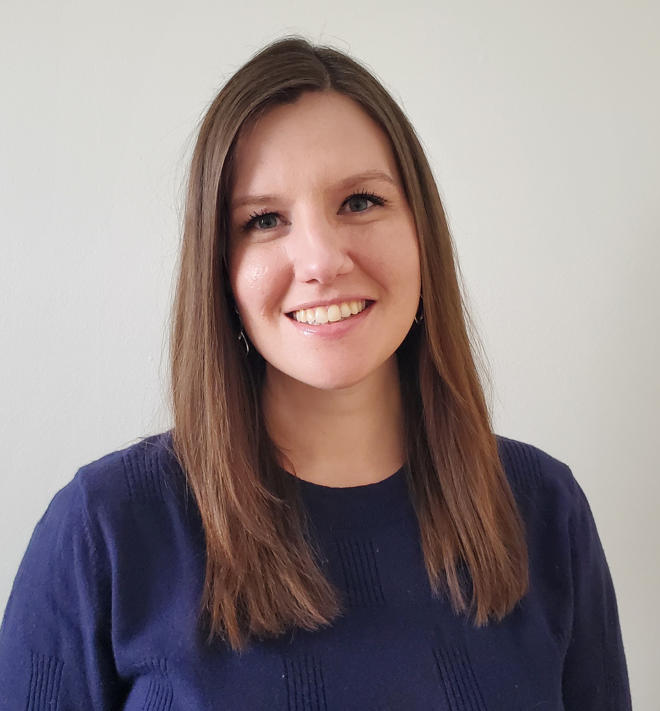 Allison Altenberger-Olson headshot. Allison poses against a neutral white background. Allison wears a navy blue blouse. Allison's brown hair falls past the shoulders.