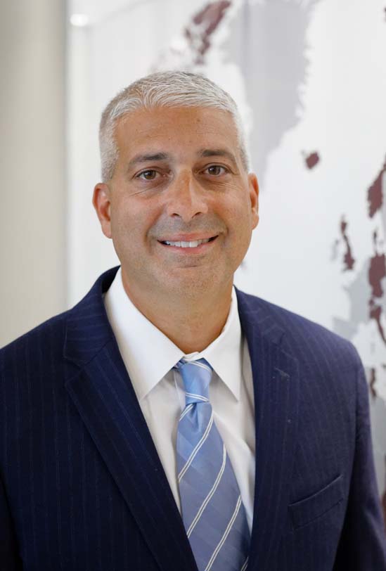 Kevin Polston poses for the camera against a neutral backdrop. Polston wears a dark suit and a light blue tie. Polston's hair is gray and is cropped close to the head. Photo by James Swoboda