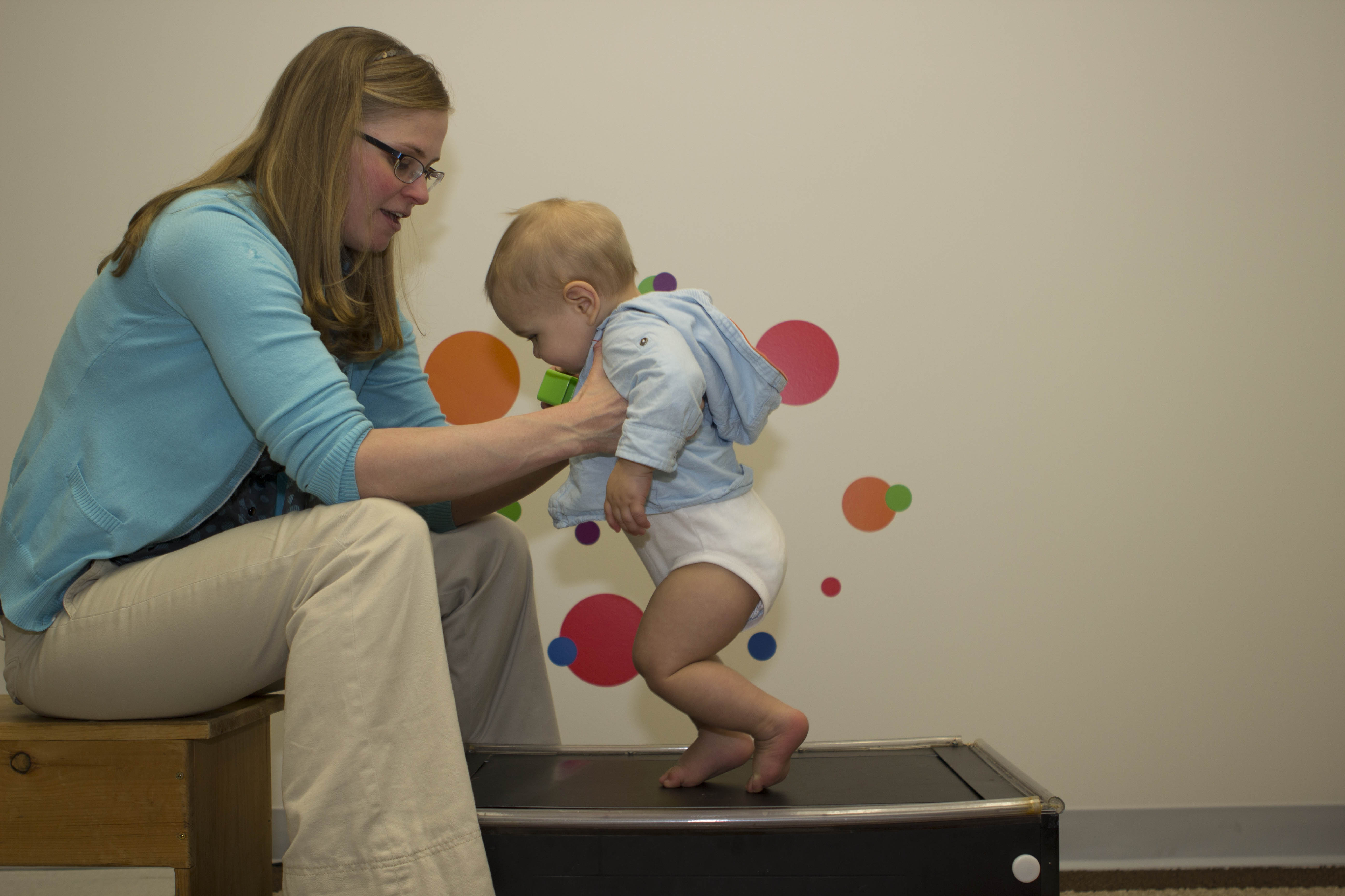 Assistant Professor Janet Hauck holds a toddler over a treadmill to help them learn to walk. 