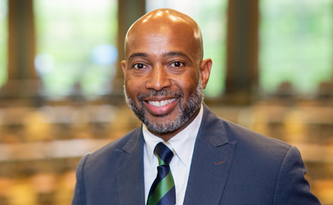 Jerlando Jackson smiles for the camera in the Erickson Hall Kiva, a circular, tiered classroom on MSU's campus. Jackson wears a white button-down shirt, a blue and green diagonally striped tie, and a dark blue blazer.