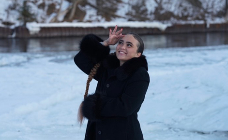 Elaine Nevins poses for the camera in the snow while wearing a black winter coat. Nevins' brown hair is in a long braid.