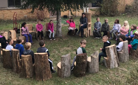 Rebecca Sandee leads students in a lesson while sitting outside on tree stumps.