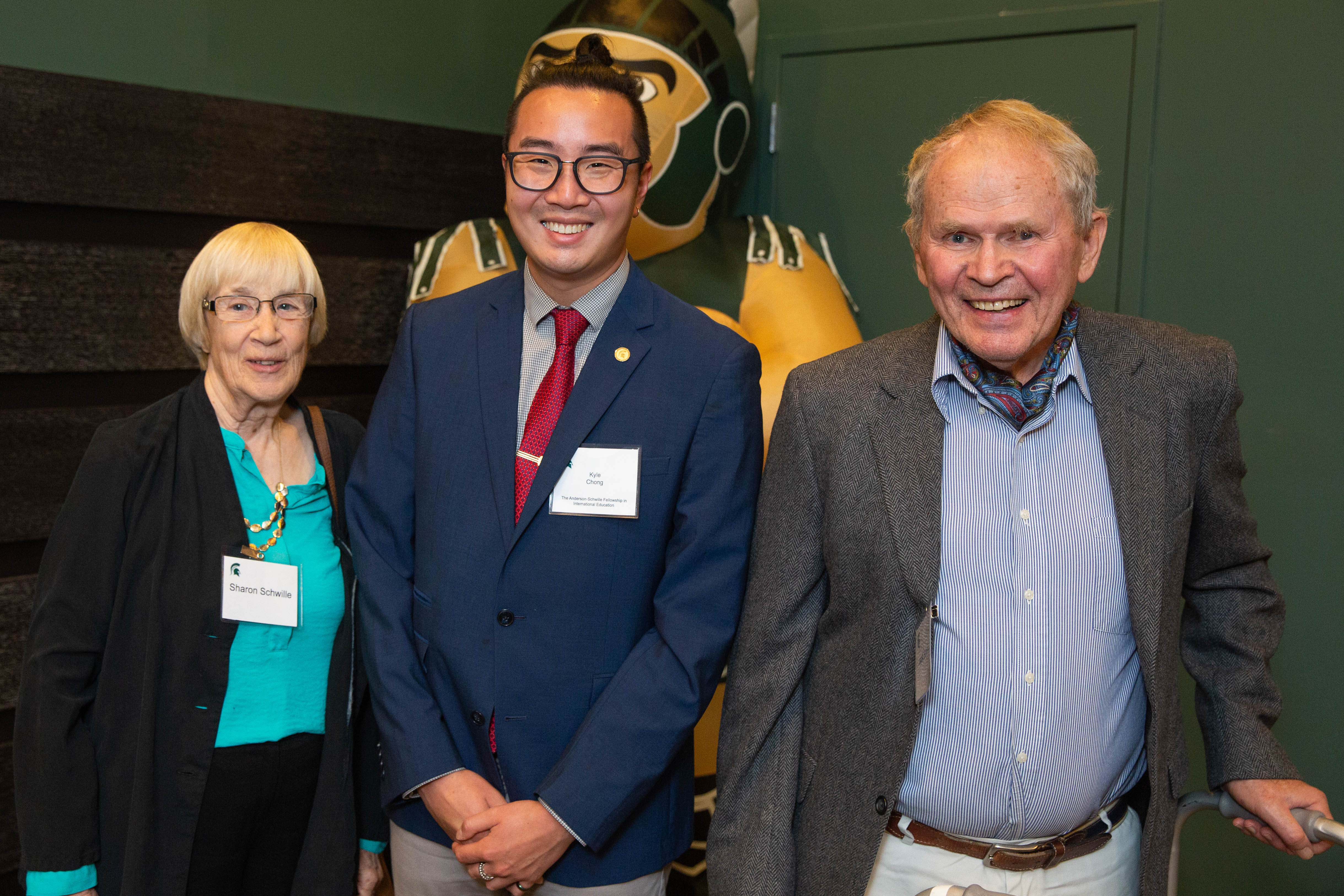 Three Spartans stand side-by-site at a celebratory event; an inflatable Sparty is behind the individuals. Sharon Schwille stands on the left, Kyle Chong stands in the middle, Jack Schwille stands on the far right.