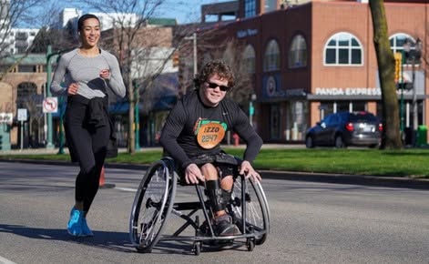 Darice Brooks runs alongside an individual on a wheelchair on MSU's campus