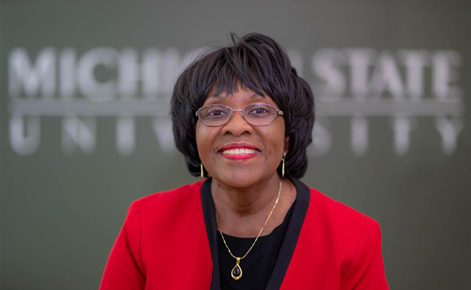 Patricia Edwards smiles toward the camera in front of a sign that reads