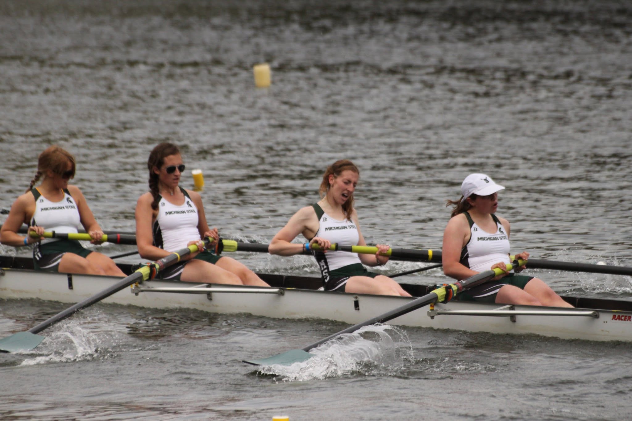 Four Spartans wearing rowing uniforms actively row during a competition.