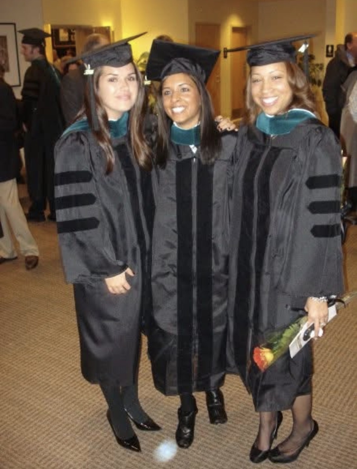 Three graduates stand and smile in doctoral regalia.