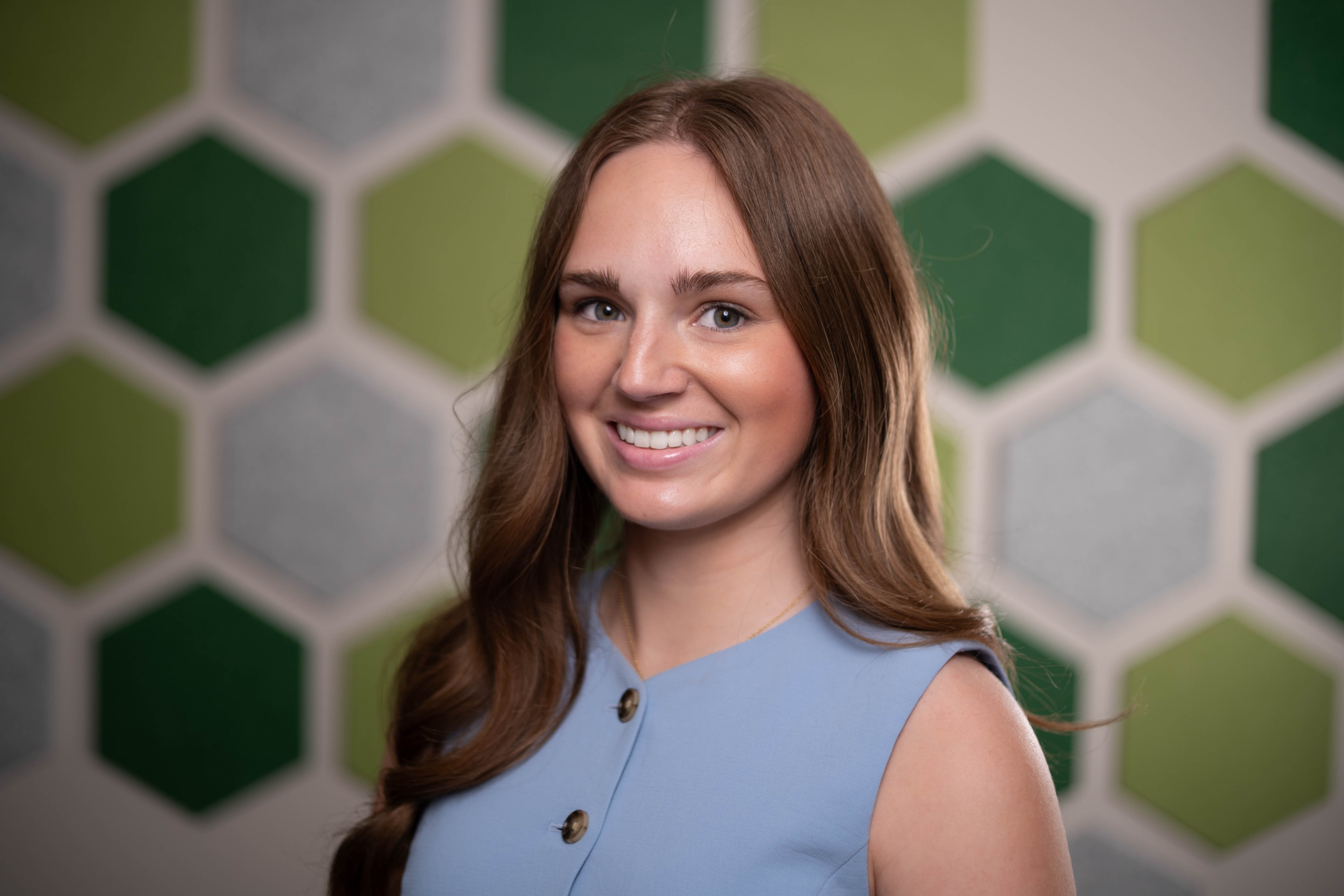 Colleen Kubisiak smiles for the camera in front of a wall filled with green and gray hexagon decals.