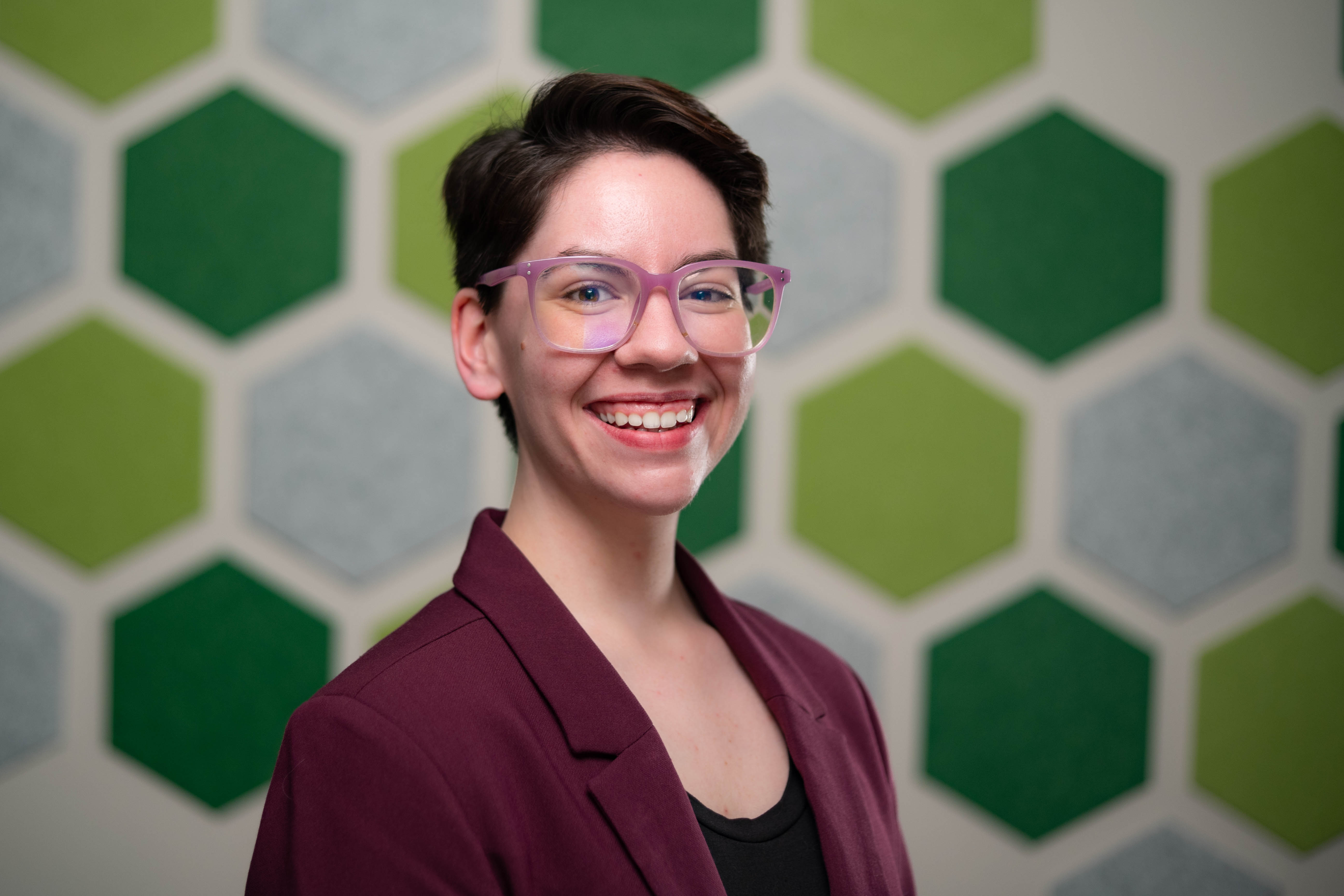 Maddie Green smiles for the camera in front of a wall filled with green and gray hexagons.