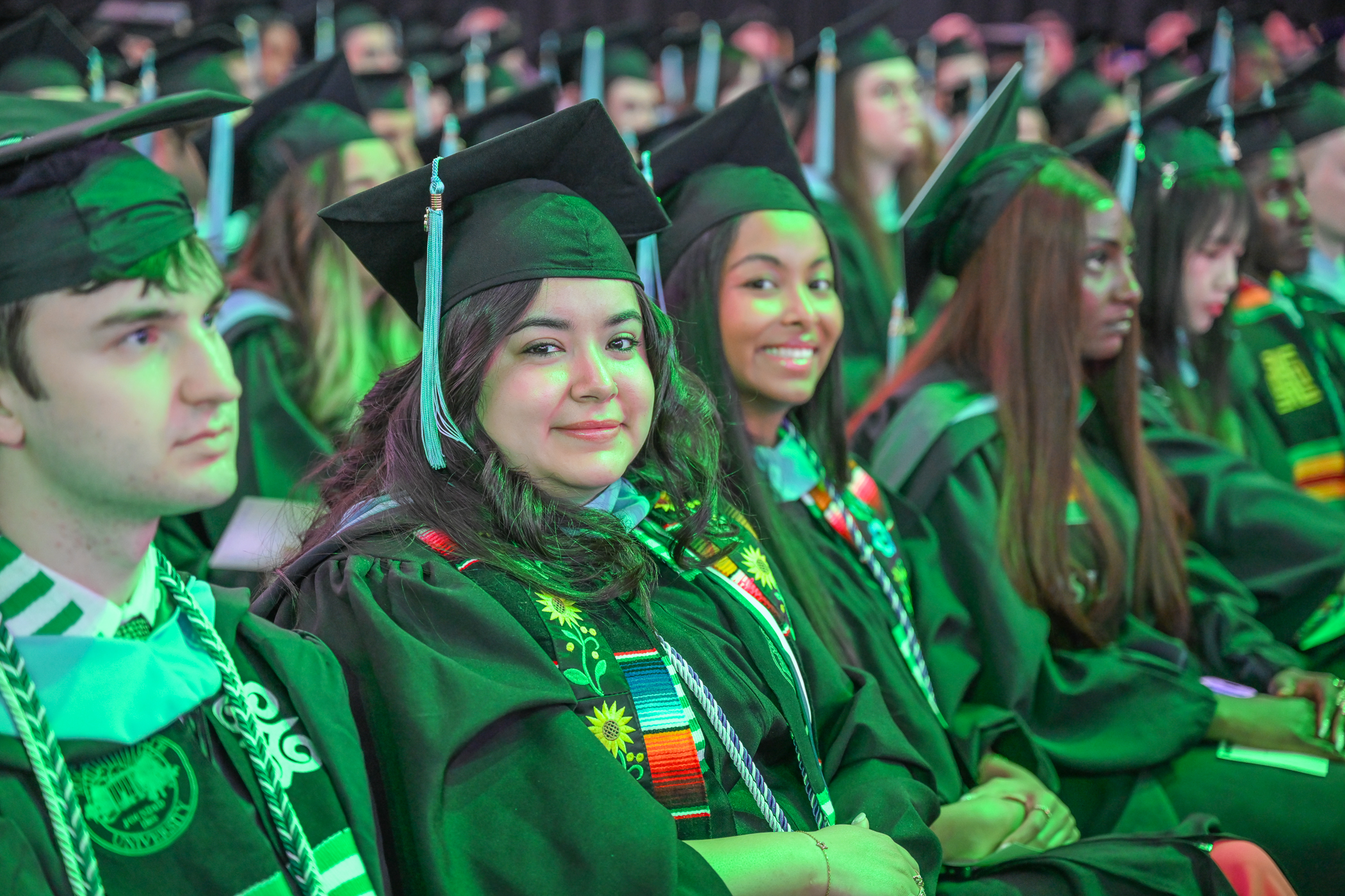 College of Education master's students smile at a graduation ceremony in gap and gown.