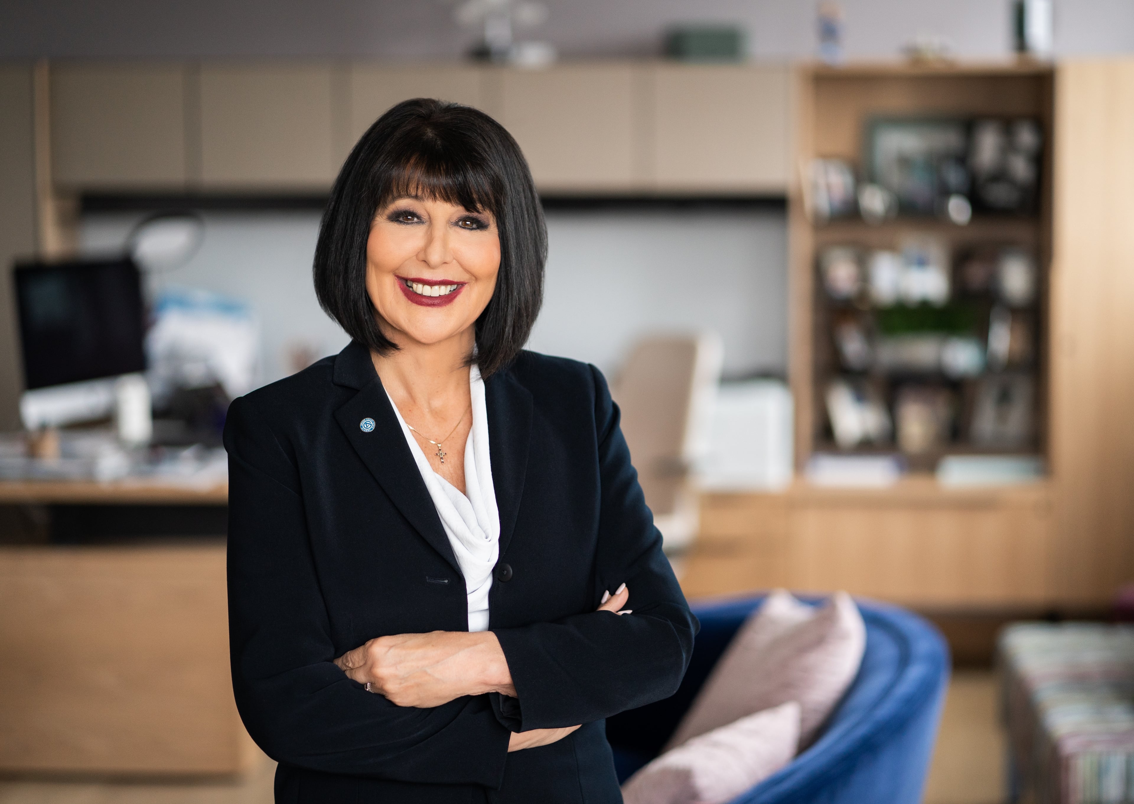 Philomena Mantella poses for a photo in an office setting while crossing arms in front of the chest. Mantella wears a dark suit with a Grand Valley State University pin. Mantella has shoulder-length black hair.