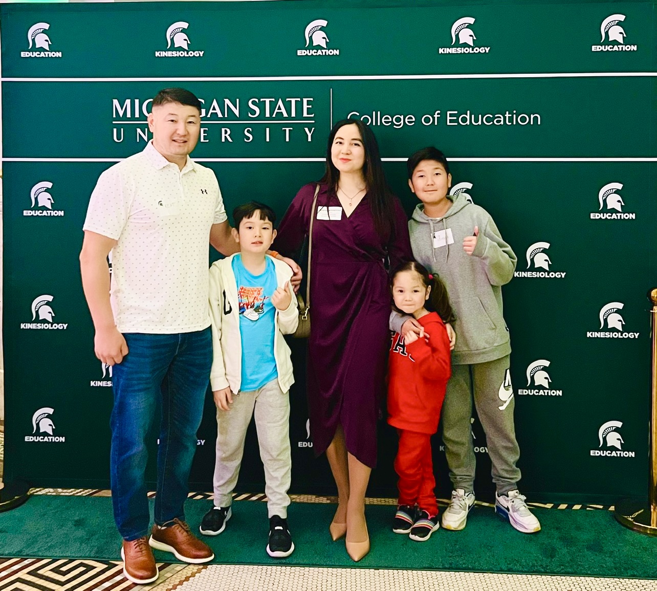 Anara Akhmetiva poses with family in front of a sign with the MSU College of Education logo.
