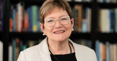 Ann Austin poses for the camera in front of a bookshelf