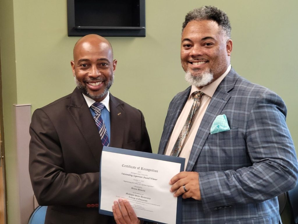 Jerlando F. L. Jackson and Bryan Beverly pose for a photo; Beverly holds a sign awarding him as an Outstanding Supervisor.