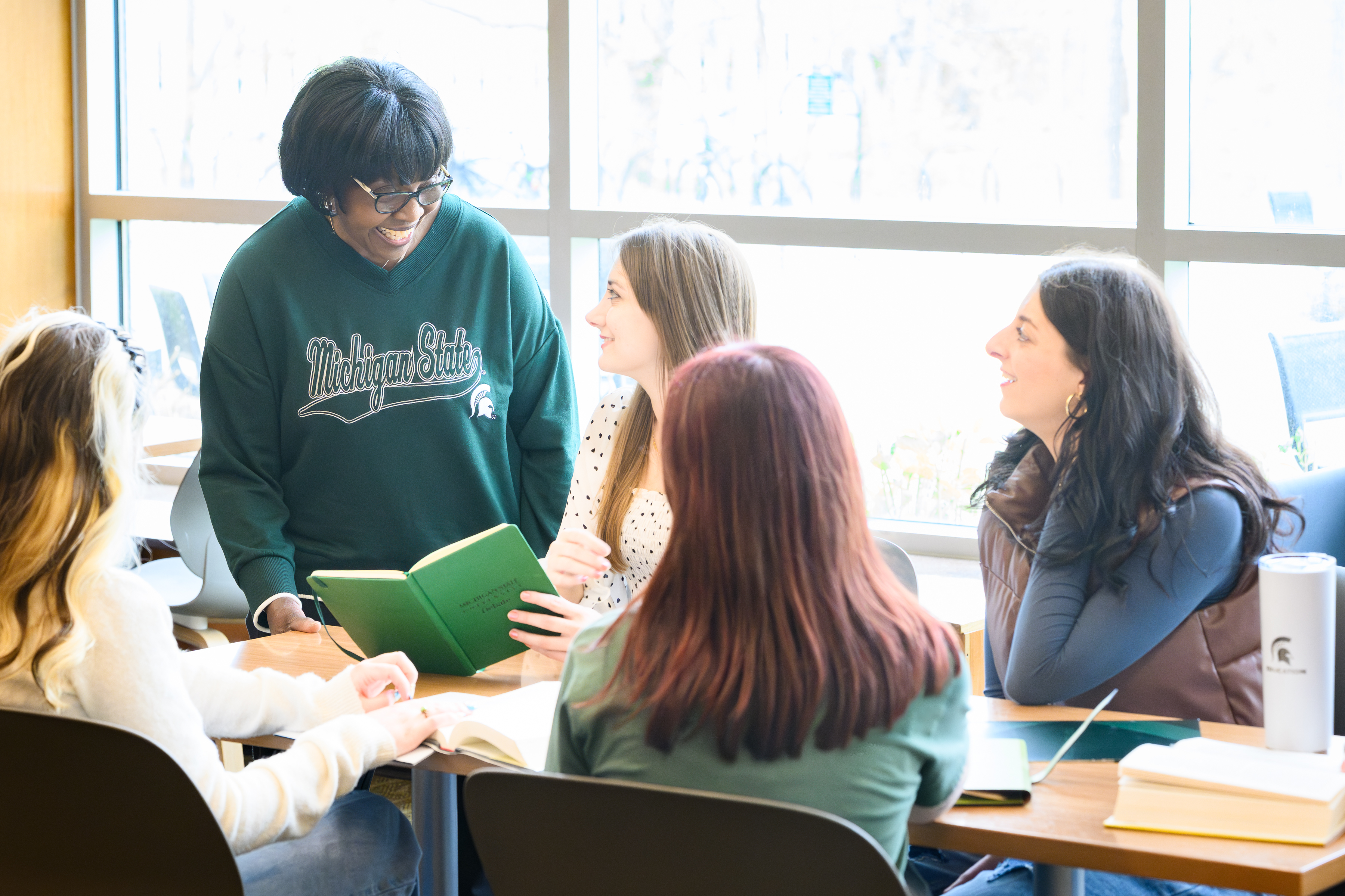 Patricia Edwards works with students in the Erickson Hall lobby. Patricia Edwards smiles while standing working with the students. 