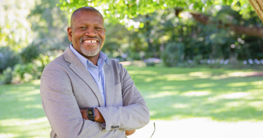 Leps Malete stands outside with arms crossed, smiling for the camera.