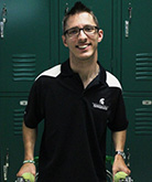 Piotr Pasik headshot. Pasik stands in front of dark green lockers and smiles for the camera. Piotr wears a black polo tee-shirt with white accents around the arms and dark-rimmed glasses. Piotr leans on two walking canes. Piotr's dark hair is short and spiky.