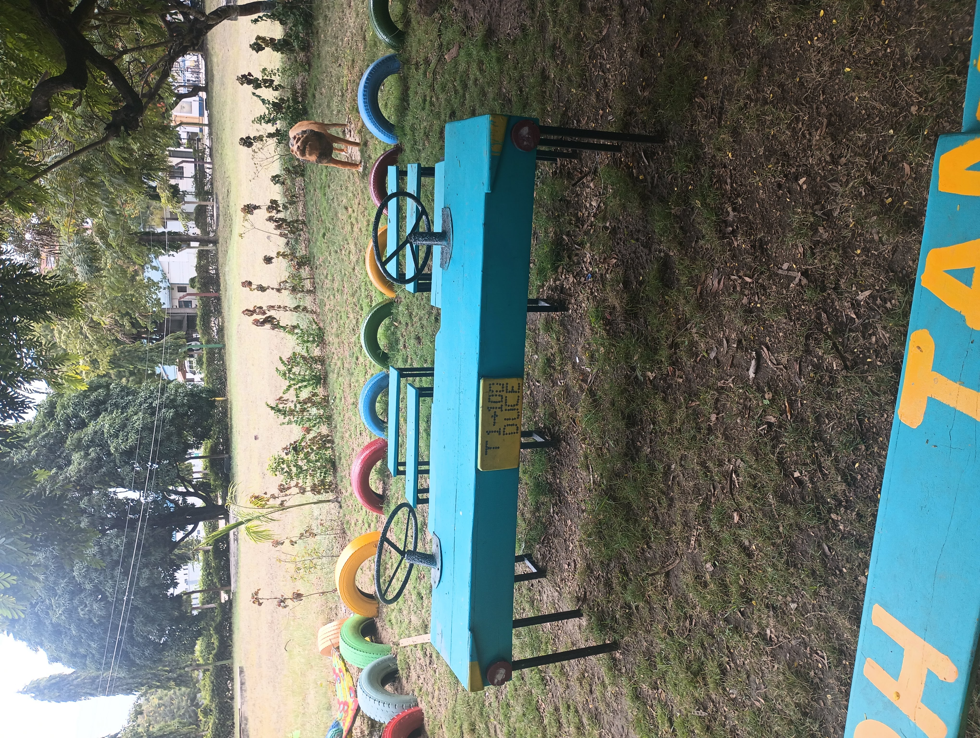 Close-up of blue tables and chairs positioned like a car or a bus. Surrounding this are tires that serve as a fence painted in rainbow colors.