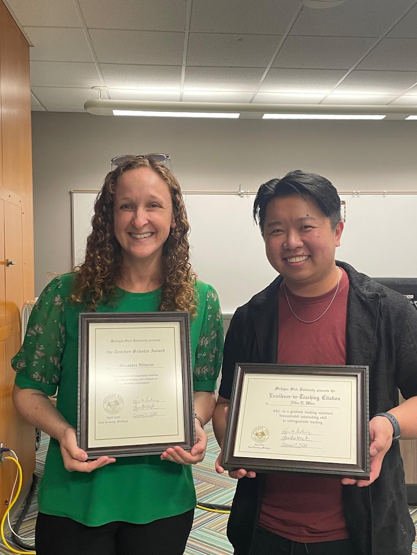 Alexandra Allweiss and E. Woo stand side-by-side, holding signs denoting their awards in the MSU All-University Awards.