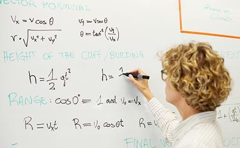 teacher writing math equations on a whiteboard