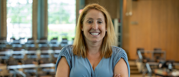 Kelley Cusmano smiles for the camera in Erickson Hall's kiva, a circular classroom. Cusmano wears a sleeveless, light blue top. Cusmano has reddish, blonde hair that is shoulder length.