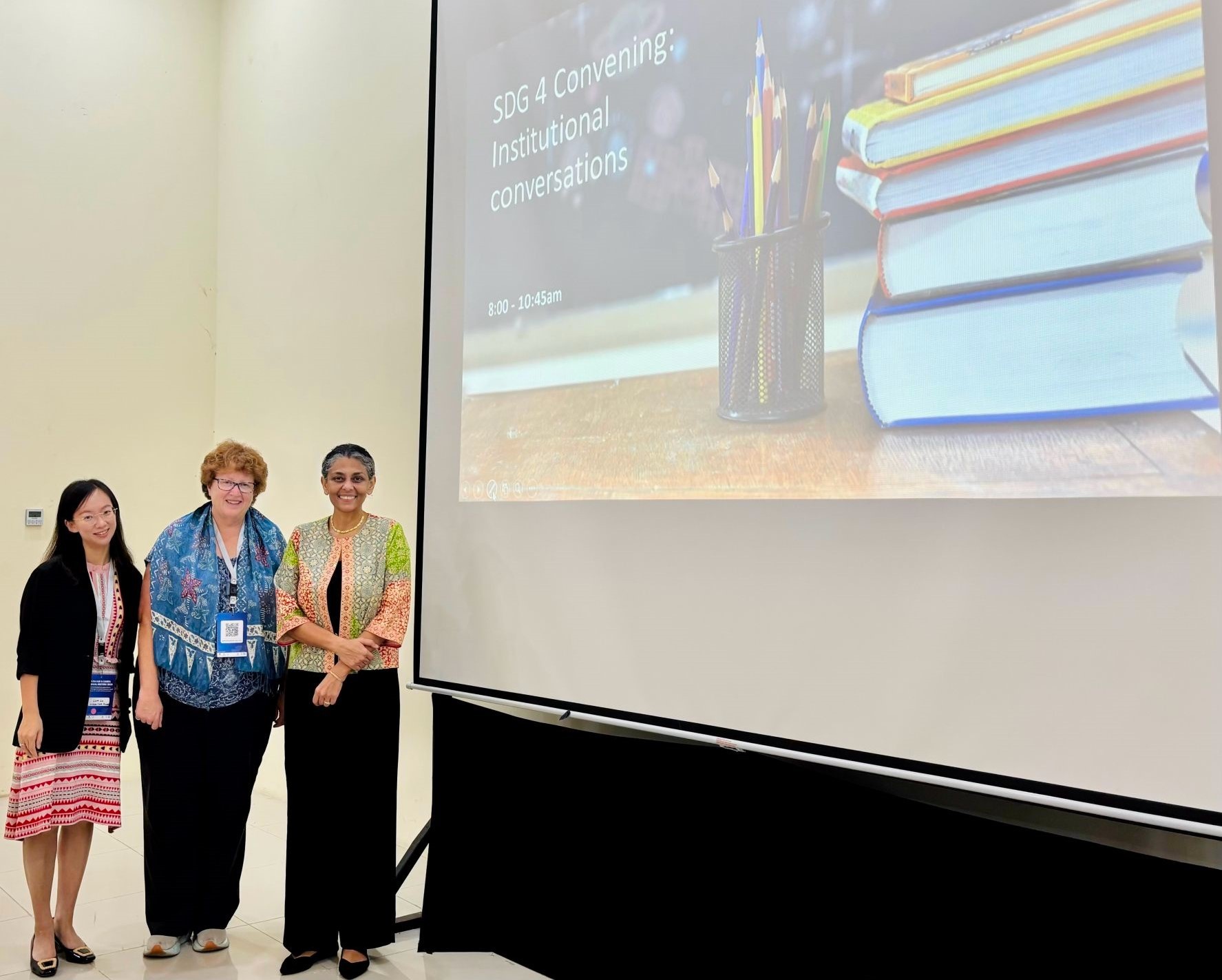 3 women standing in front of a projector with a slideshow called "SDG 4 Convening: Institutional conversations"