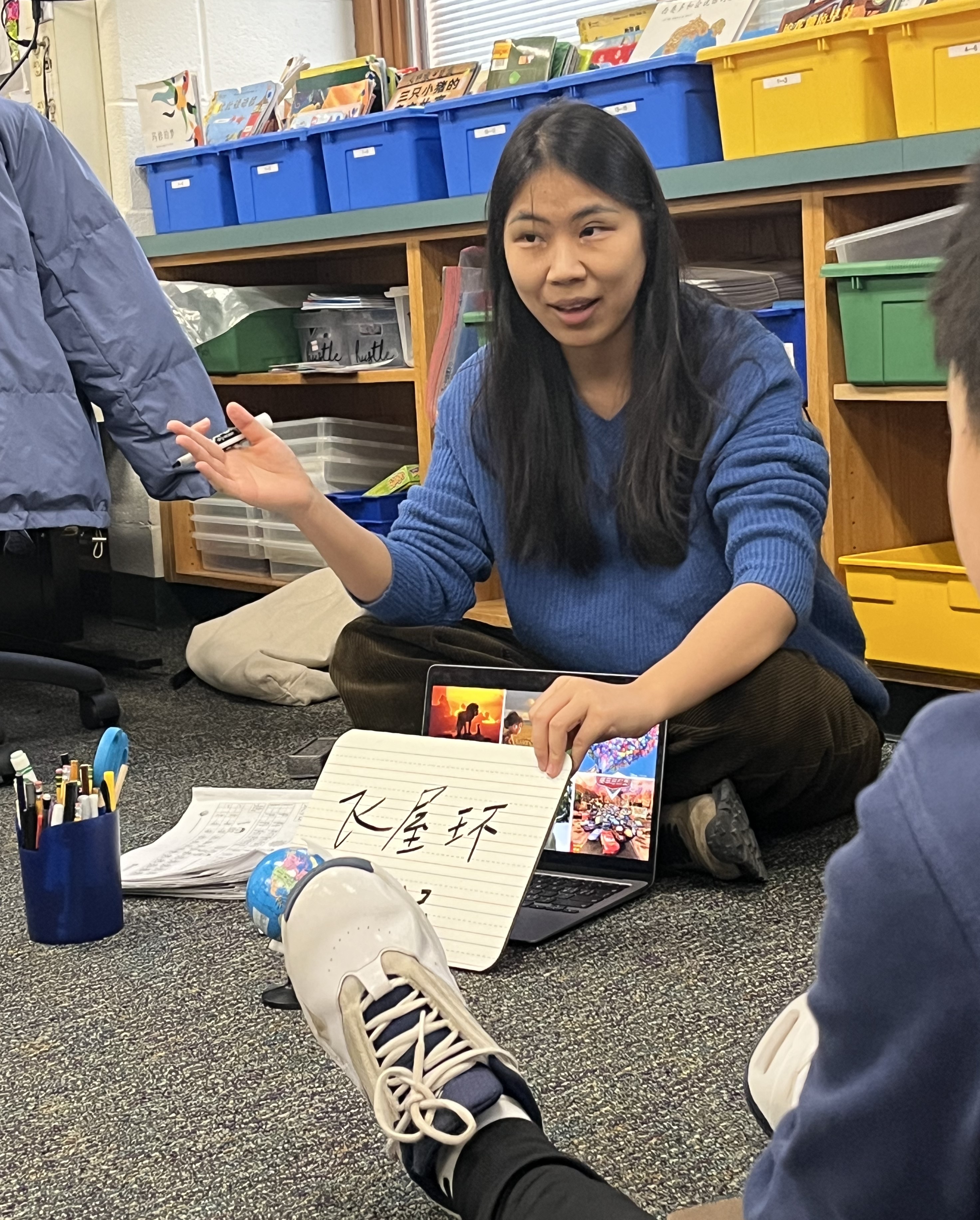 woman teaching children in a classroom a language written on a notepad